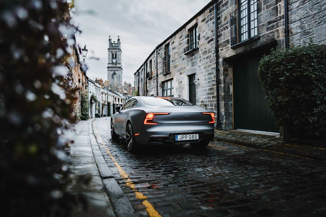 A grey Polestar 1 driving on a narrow cobblestone street.