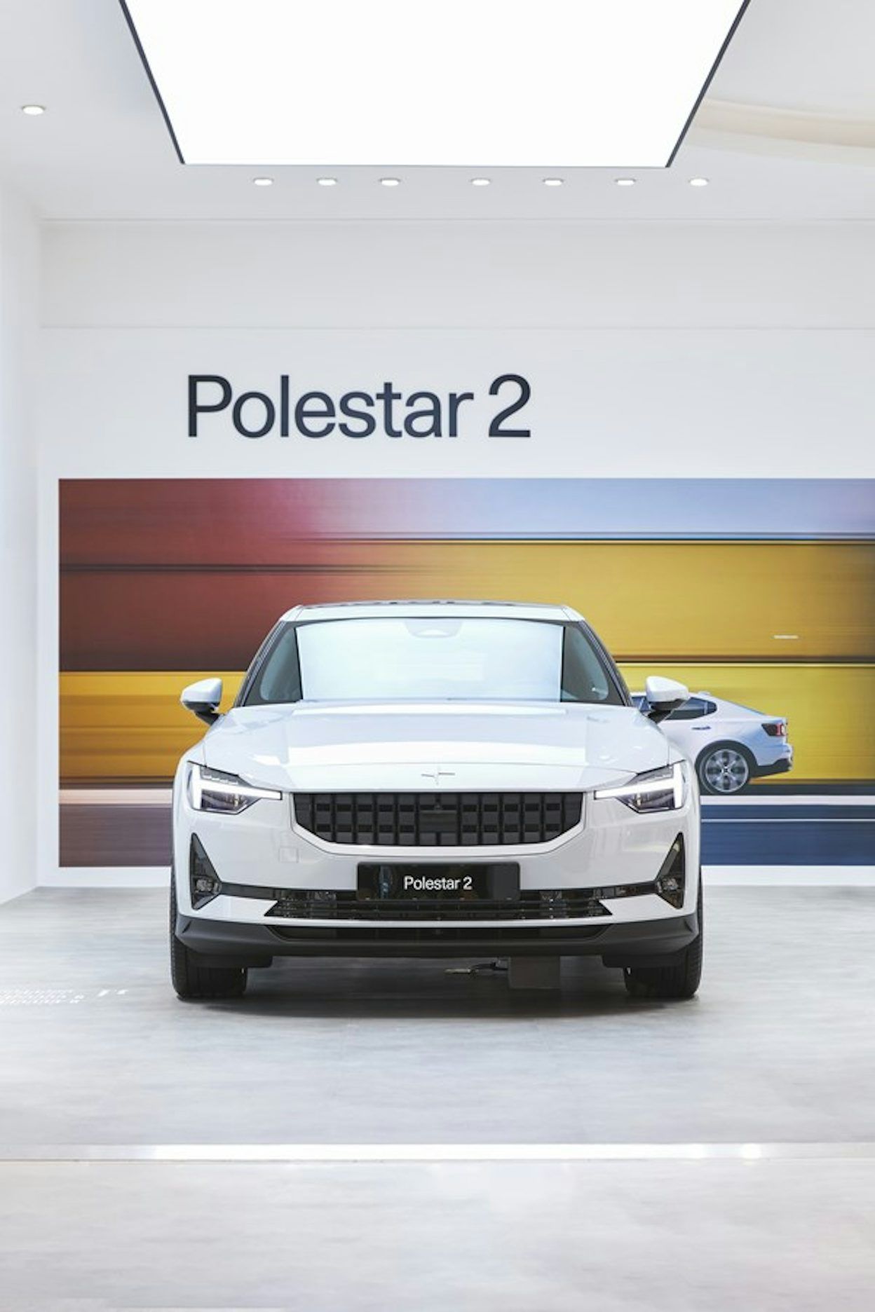 White Polestar 2 seen from the front. Colourful blurry image on the wall behind it.