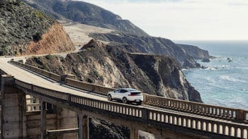 Polestar 3 from afar driving over a bridge overlooking the ocean.