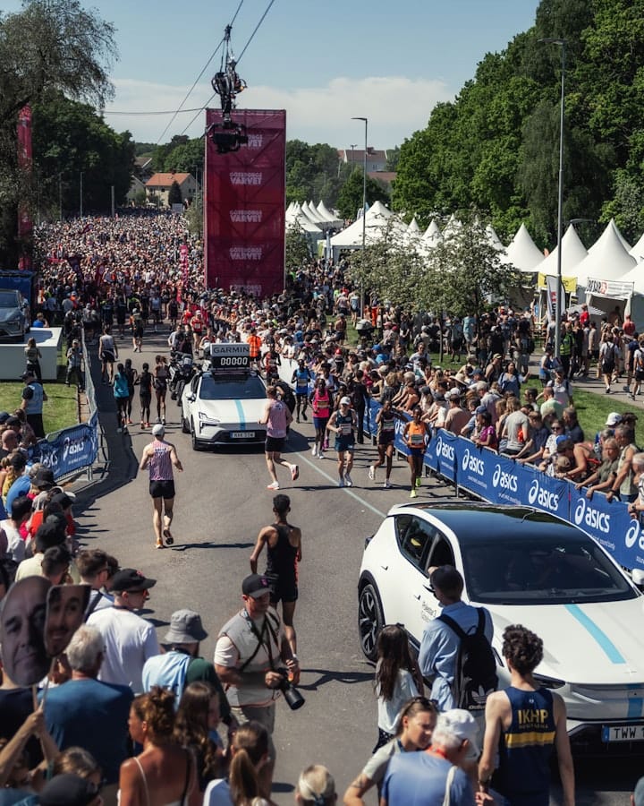 A Polestar 3 and a Polestar 4 parked in the starting area of the Göteborgsvarvet, with runners preparing for the race and surrounded by spectators watching the event