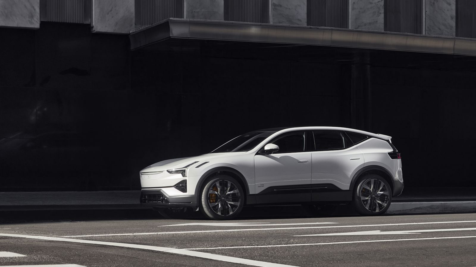 A white Polestar 3 SUV is parked on a street in front of a tall building with a dark facade.