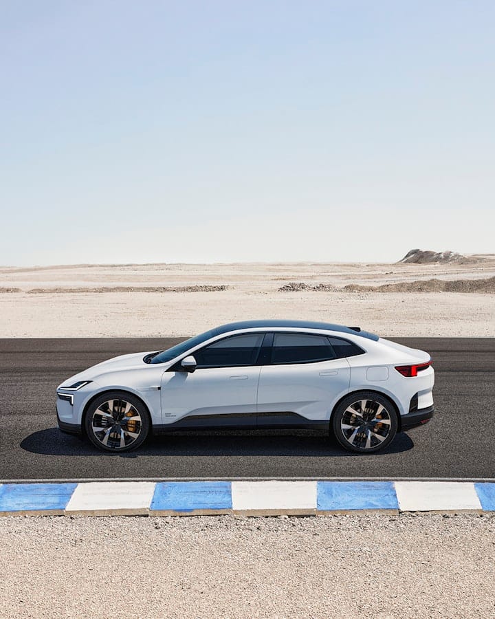 A white Polestar 4 electric SUV coupé is parked on a desert road next to a blue and white curb on a clear day.