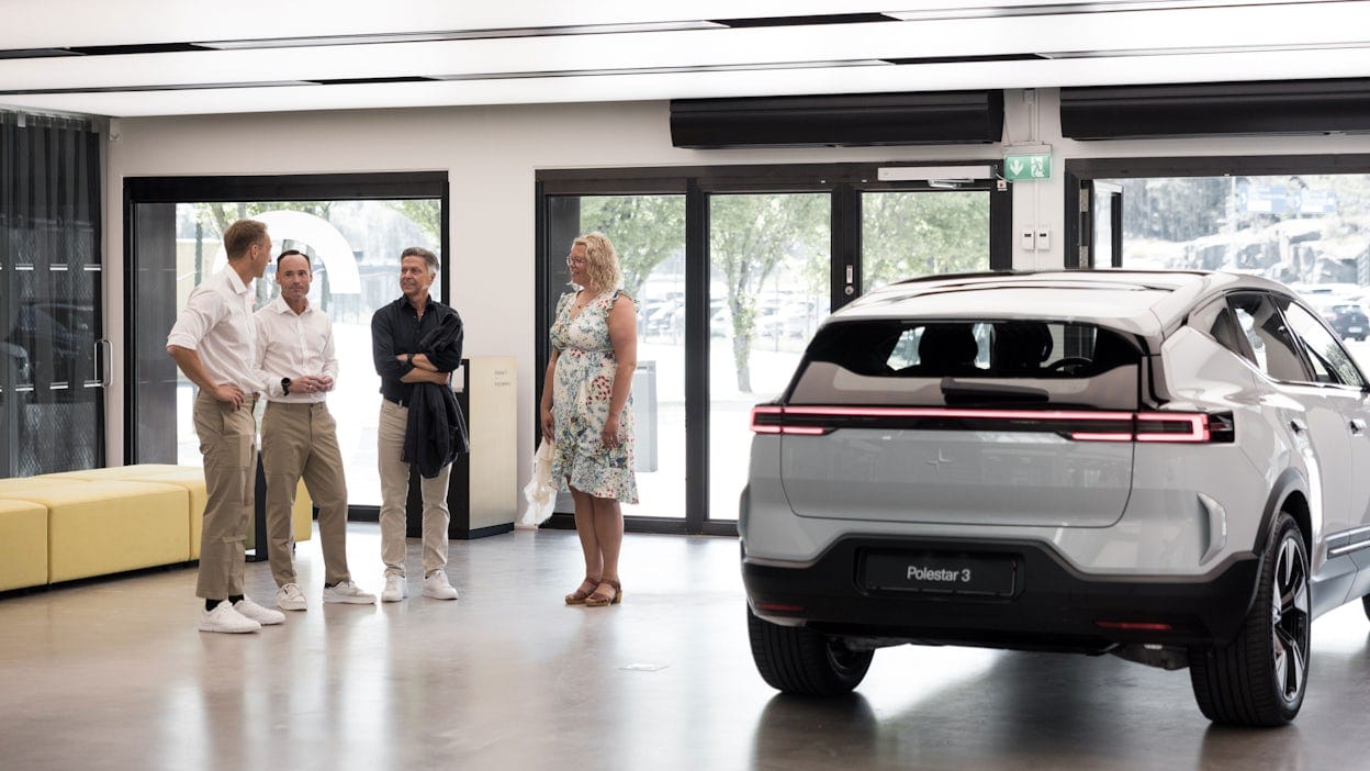 Four people talking inside Polestar HQ with the rear of a Polestar 3 visible on the right