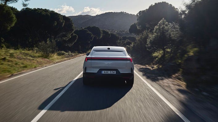 Media test driving a Polestar 4 in Spain on a straight asphalt road surrounded by forest