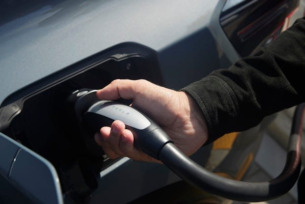 A hand plugs a charging cable into a Polestar 3 electric vehicle's charging port.