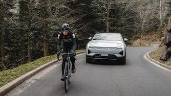 Demi Vollering fietst op de weg, op de achtergrond rijdt een Polestar 3